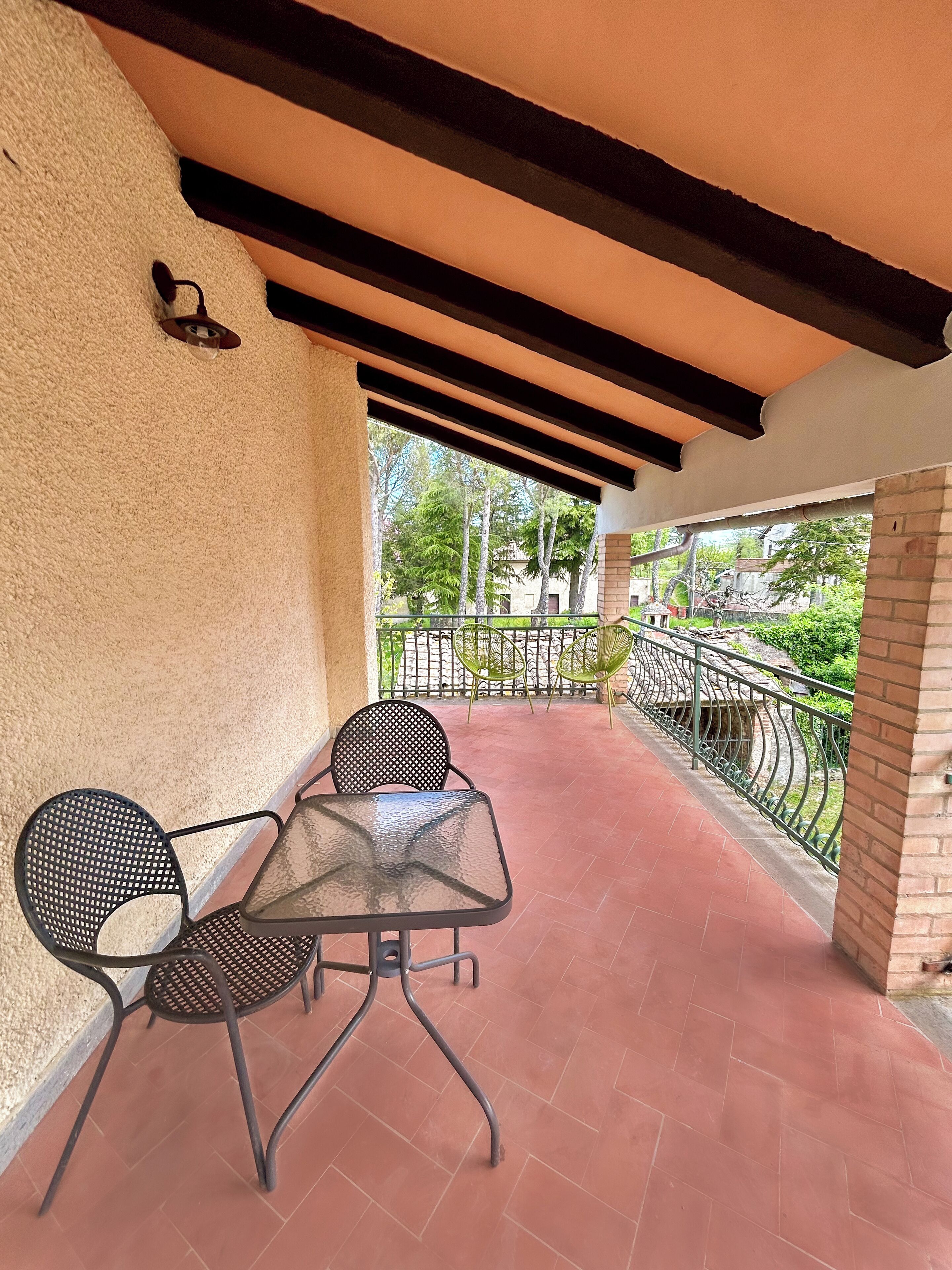 Un patio techado con mesa y sillas, vistas del entorno y una barandilla.