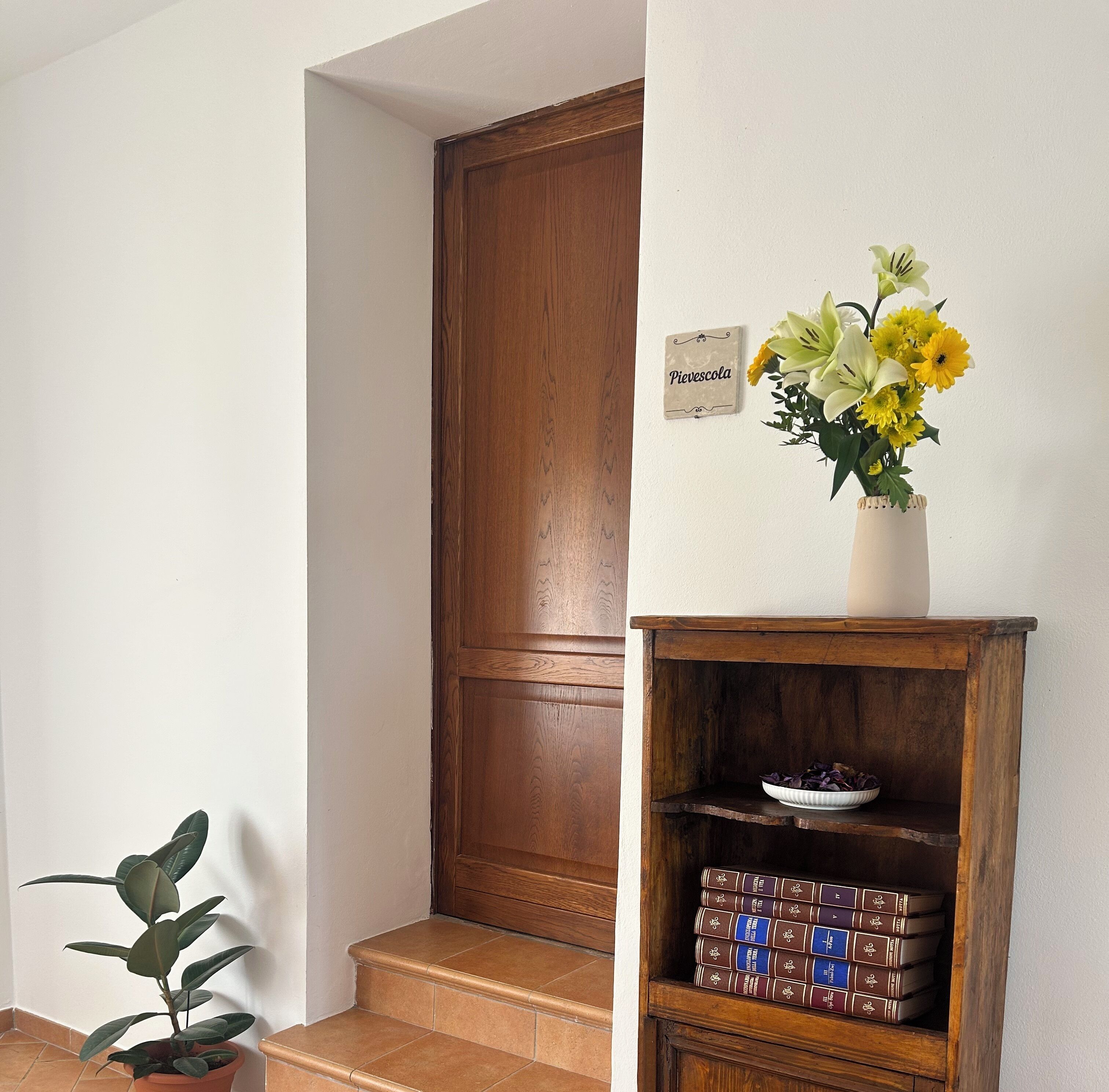 Eine Holztür, ein kleiner Topfpflanze, eine Vase mit Blumen und ein Bücherregal aus Holz.