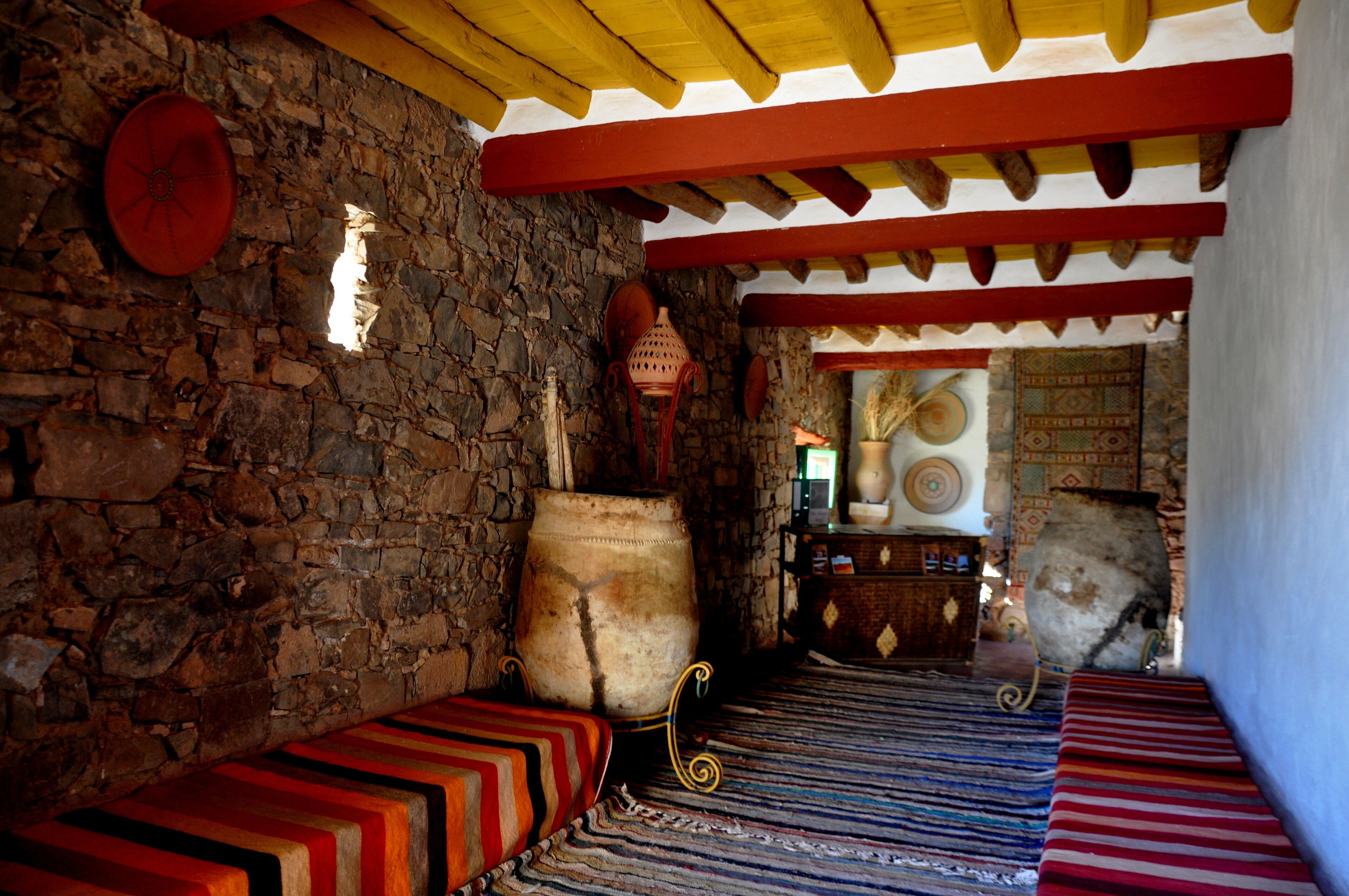 A traditional room with stone walls, a wooden ceiling, and colorful striped benches.