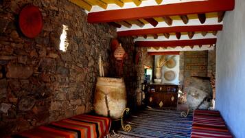 A traditional room with stone walls, a wooden ceiling, and colorful striped benches.