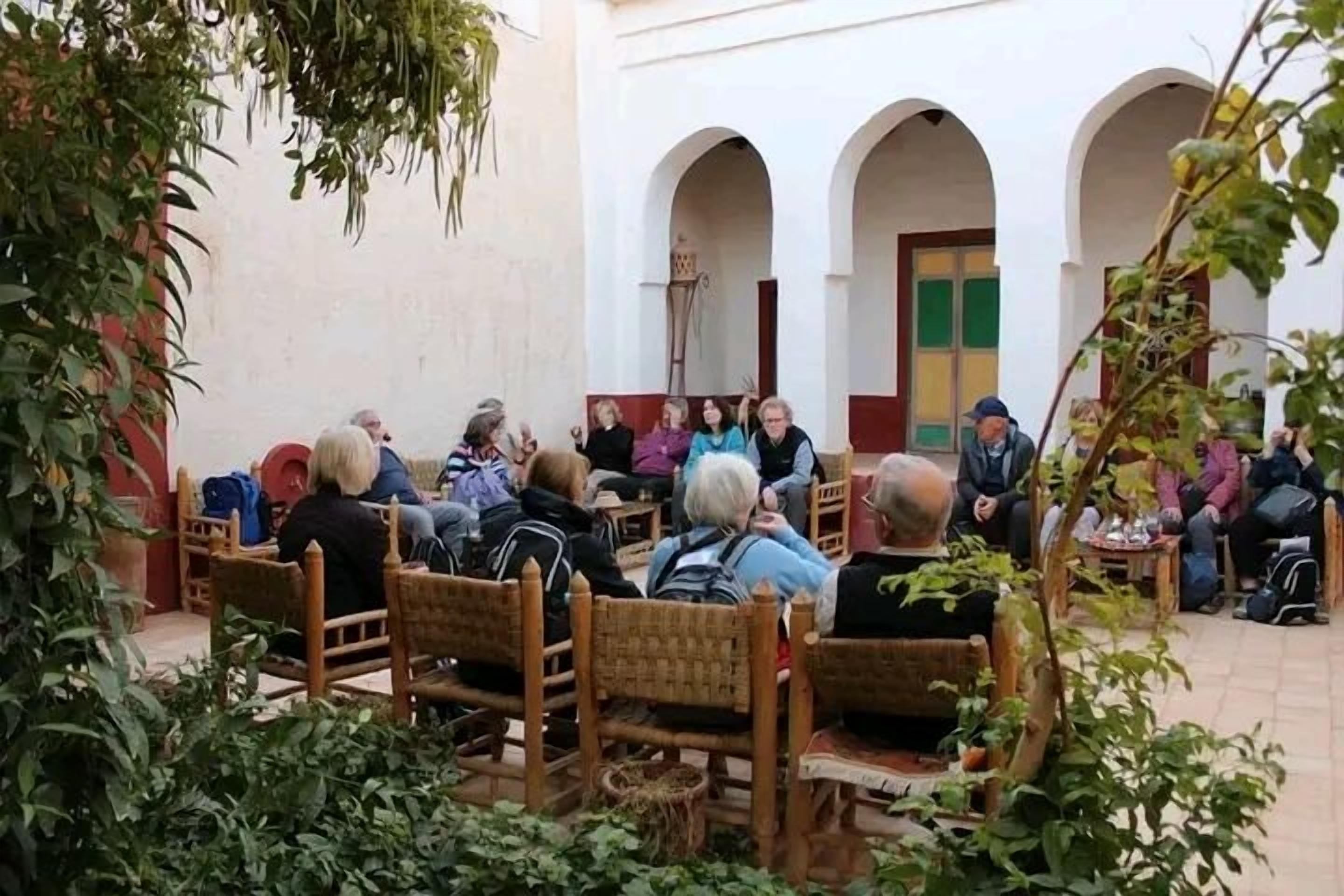 A courtyard with people seated at tables, surrounded by arches and greenery.