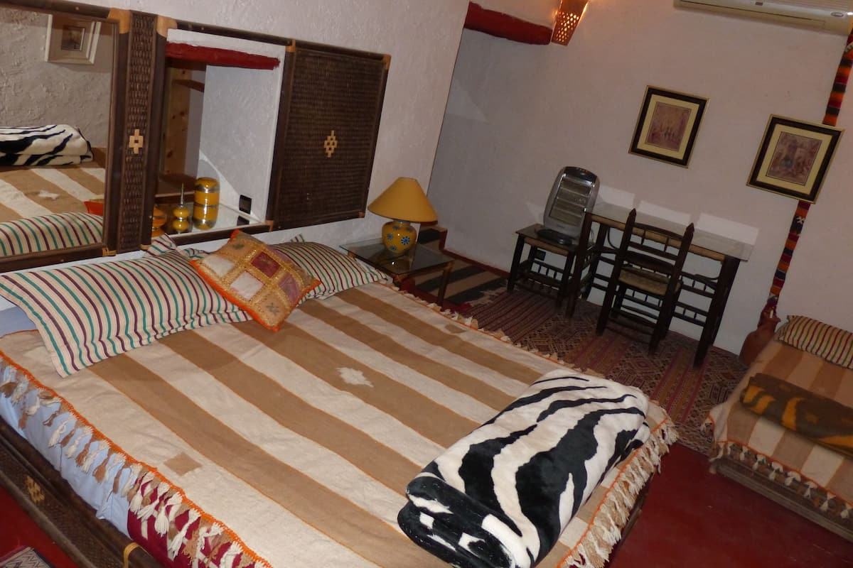 A bedroom with a large bed, a desk with a chair, a mirror, and a wall-mounted heater.