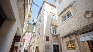 A narrow street with stone buildings, signs for a restaurant and a jewelry store, and a clear blue sky. - Stephane City Vibe Suites (Trogir)