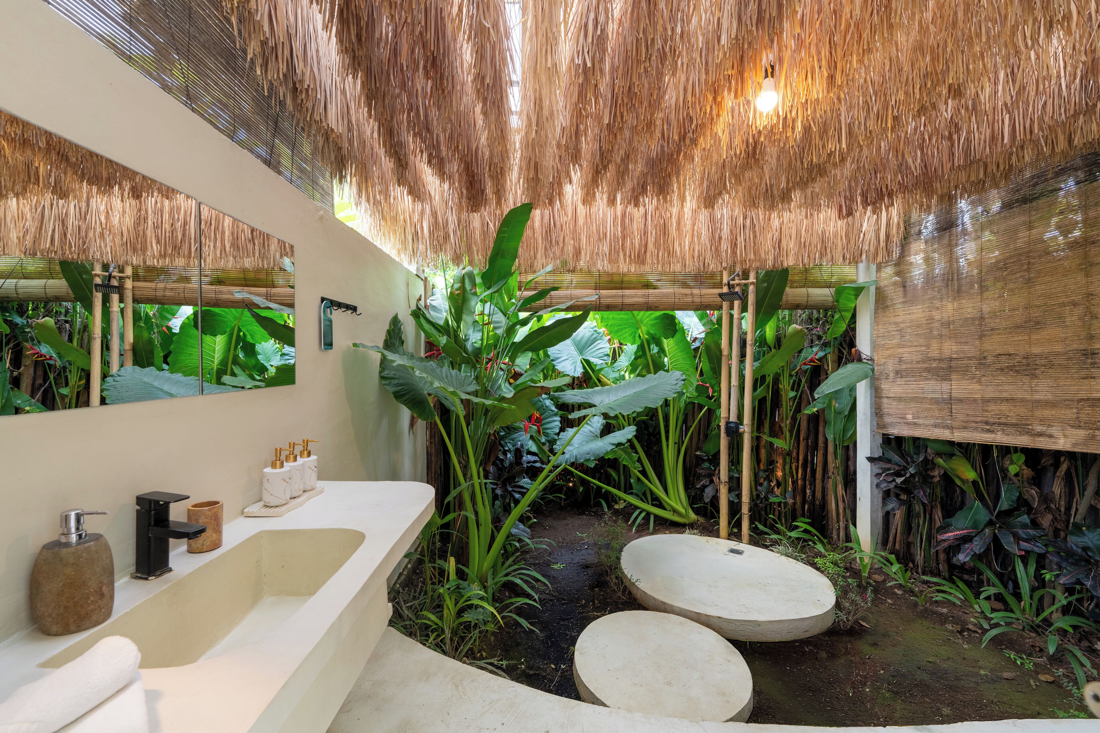 A bathroom with a large mirror, a white sink, a black faucet, and a wooden bench.