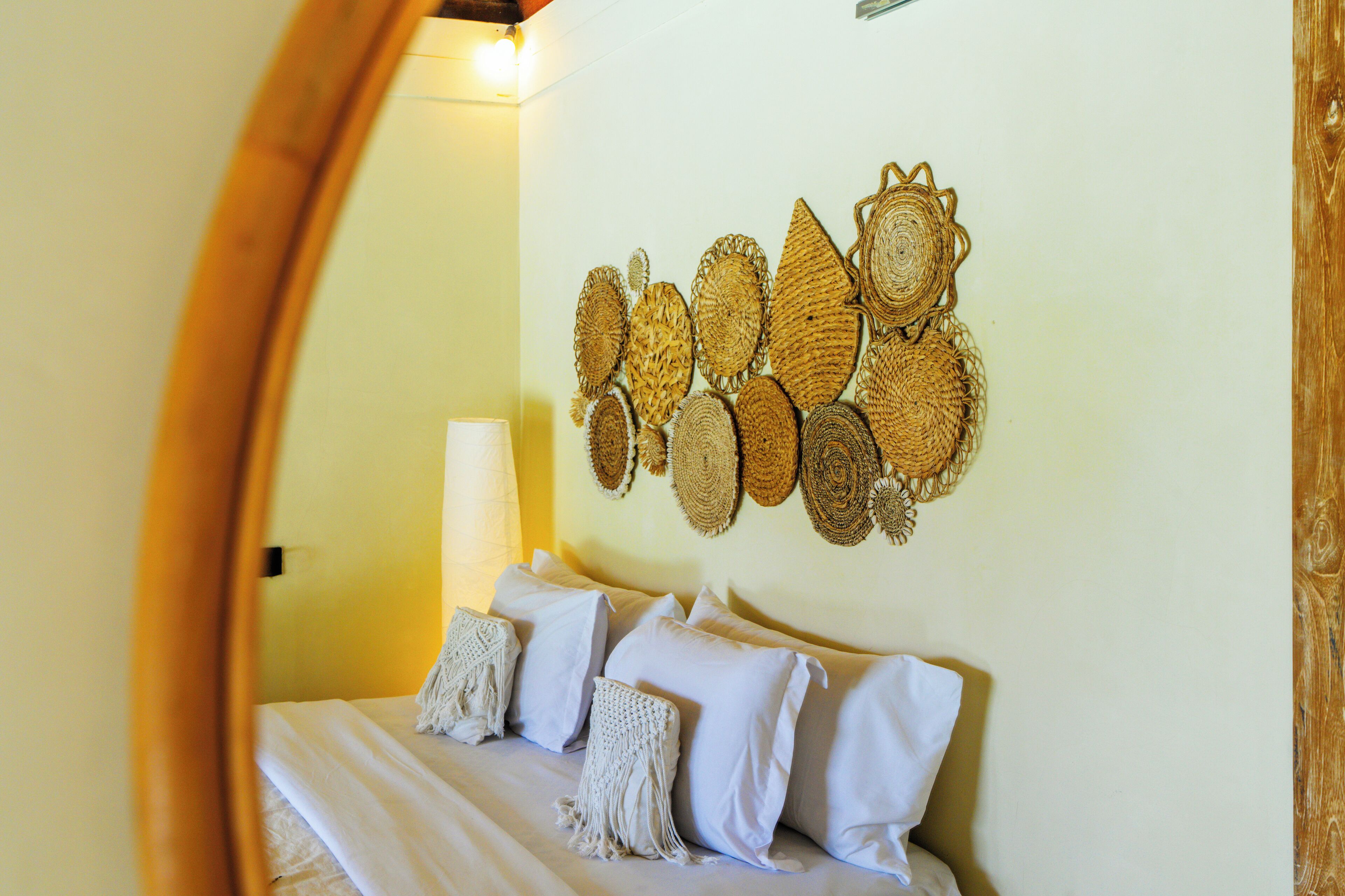 A bedroom with a bed, pillows, and a wall decorated with woven wall art.