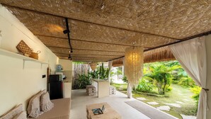 Ein Zimmer mit gewebter Decke, einem Sofa mit Makramee-Kissen, einem Holztisch und Blick auf einen Garten mit Wasserspiel.
