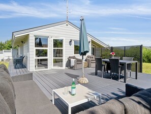 A spacious outdoor deck with a white building in the background, furnished with outdoor seating and a table.