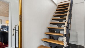 A staircase with wooden steps and a rope handrail, leading to a room with a large mirror and a red carpet.