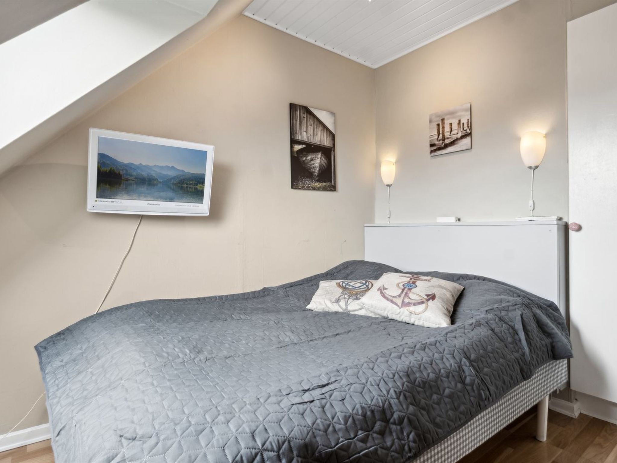 Quarto com cama, televisão fixada na parede e duas luminárias.