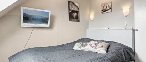 A bedroom with a bed, a TV mounted on the wall, and two wall-mounted lamps.