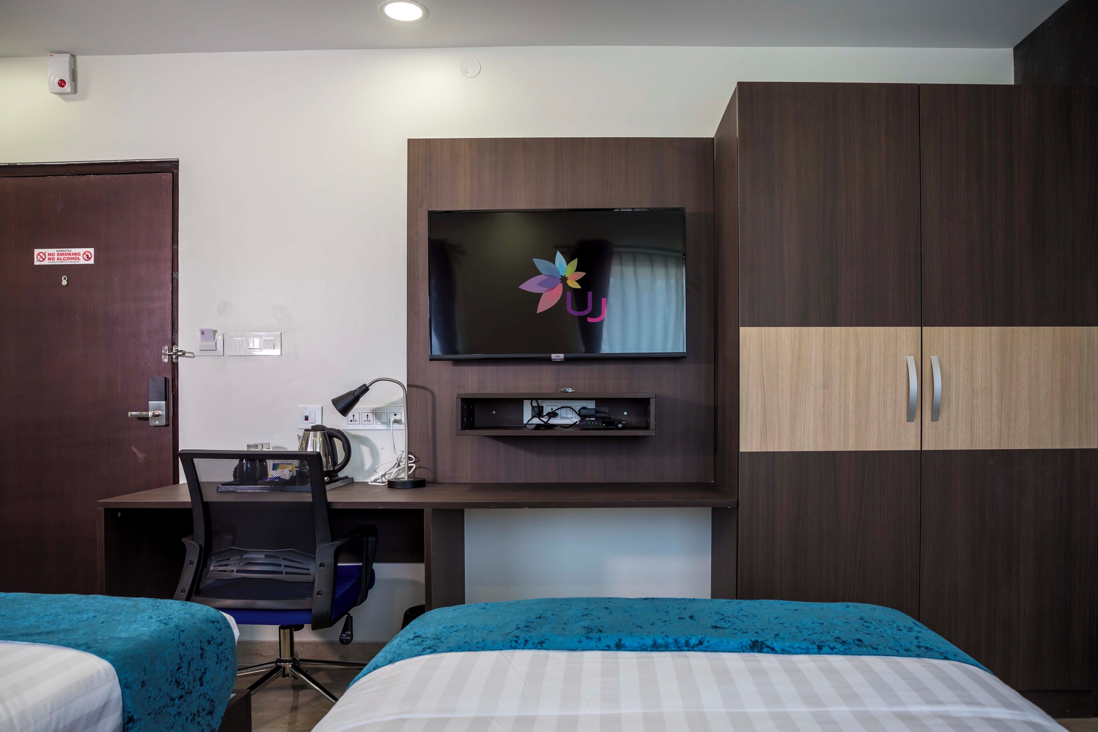 Camera d'albergo con due letti, una scrivania con un computer, una TV a parete e un armadio.