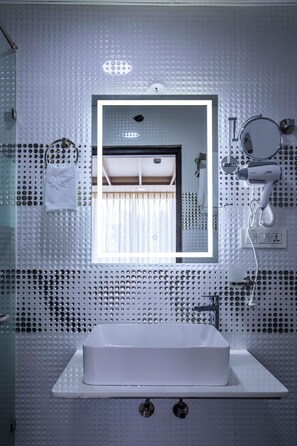 Ein modernes Badezimmer mit einem großen rechteckigen Spiegel, einem weißen Waschbecken und einem an der Wand befestigten Föhn.