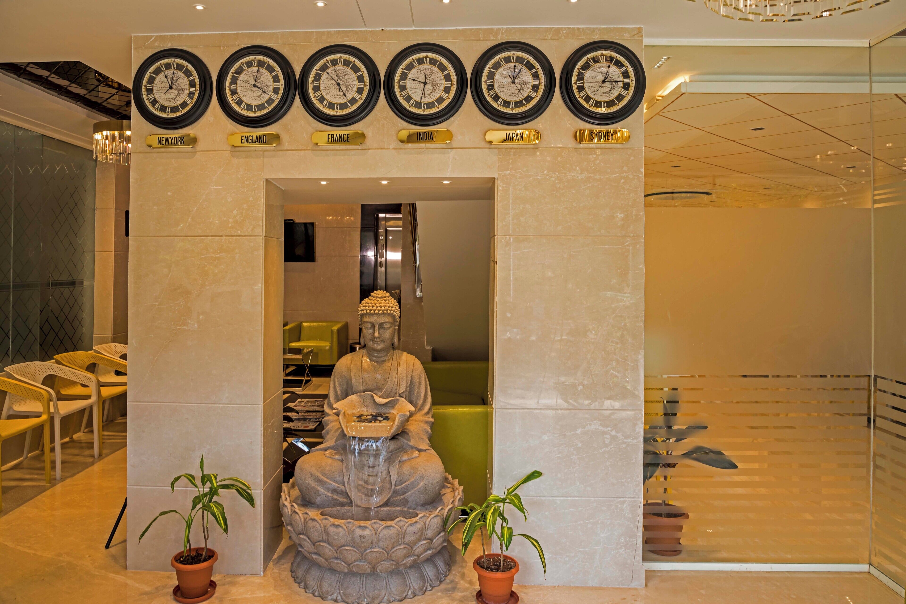 A Buddha statue with a water feature in front, surrounded by potted plants.