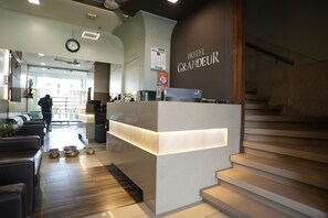 Et hotelreceptionsområde med moderne design, en receptionsdisk, en trappe og udsigt over lobbyen.