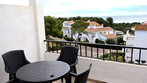 Un balcón con una mesa redonda y sillas, con vista a una zona residencial con casas y al mar.