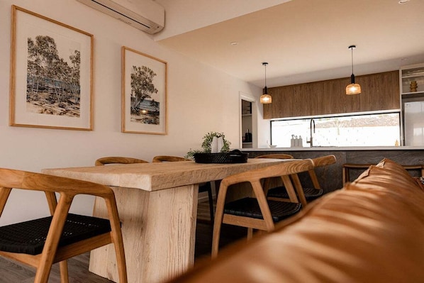 A modern dining area with a wooden table and chairs, framed artwork on the wall, and pendant lighting.