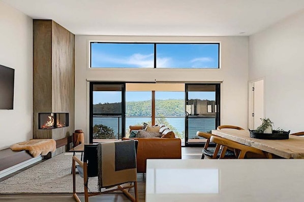 A modern interior with a fireplace, seating area, and large windows overlooking a scenic landscape.