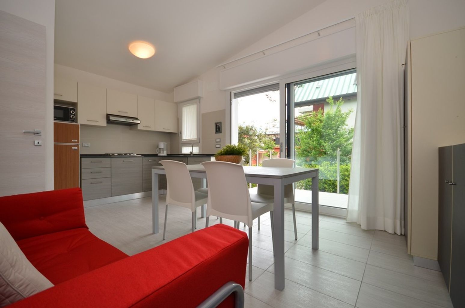 A modern kitchen with white cabinets, a dining area with a table and chairs, and a red sofa.