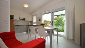 A modern kitchen with white cabinets, a dining area with a table and chairs, and a red sofa.