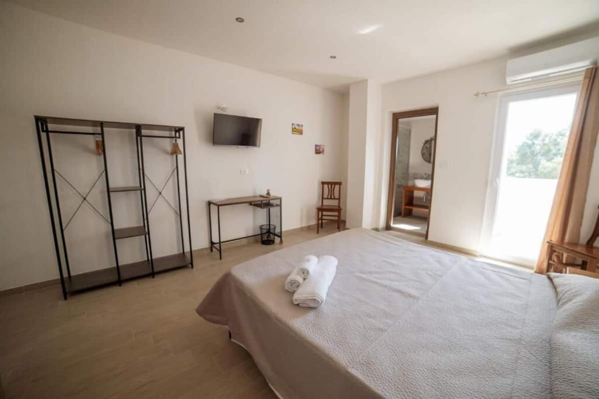 A hotel room with a large bed, a TV mounted on the wall, a desk, and a wardrobe.