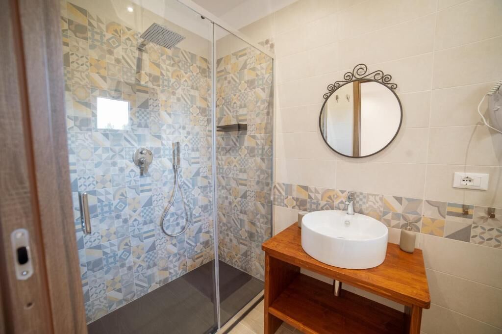 Un baño con ducha de vidrio, un espejo redondo y un tocador de madera con lavamanos blanco.