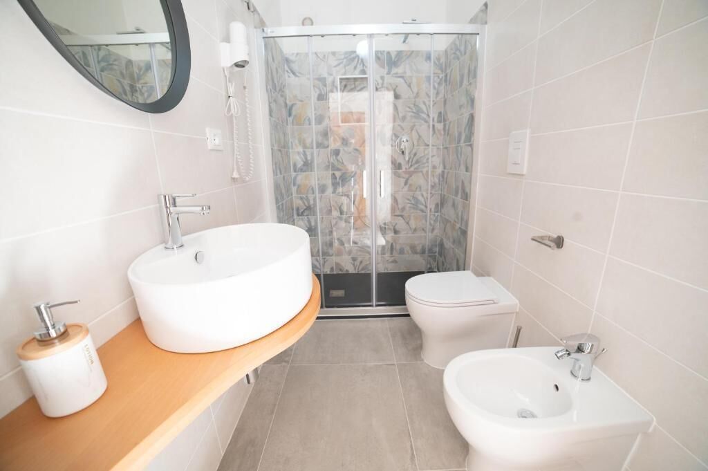 Ein modernes Badezimmer mit einem großen runden Waschbecken, einem kleinen Waschbecken, einem Bidet und einer Duschkabine.