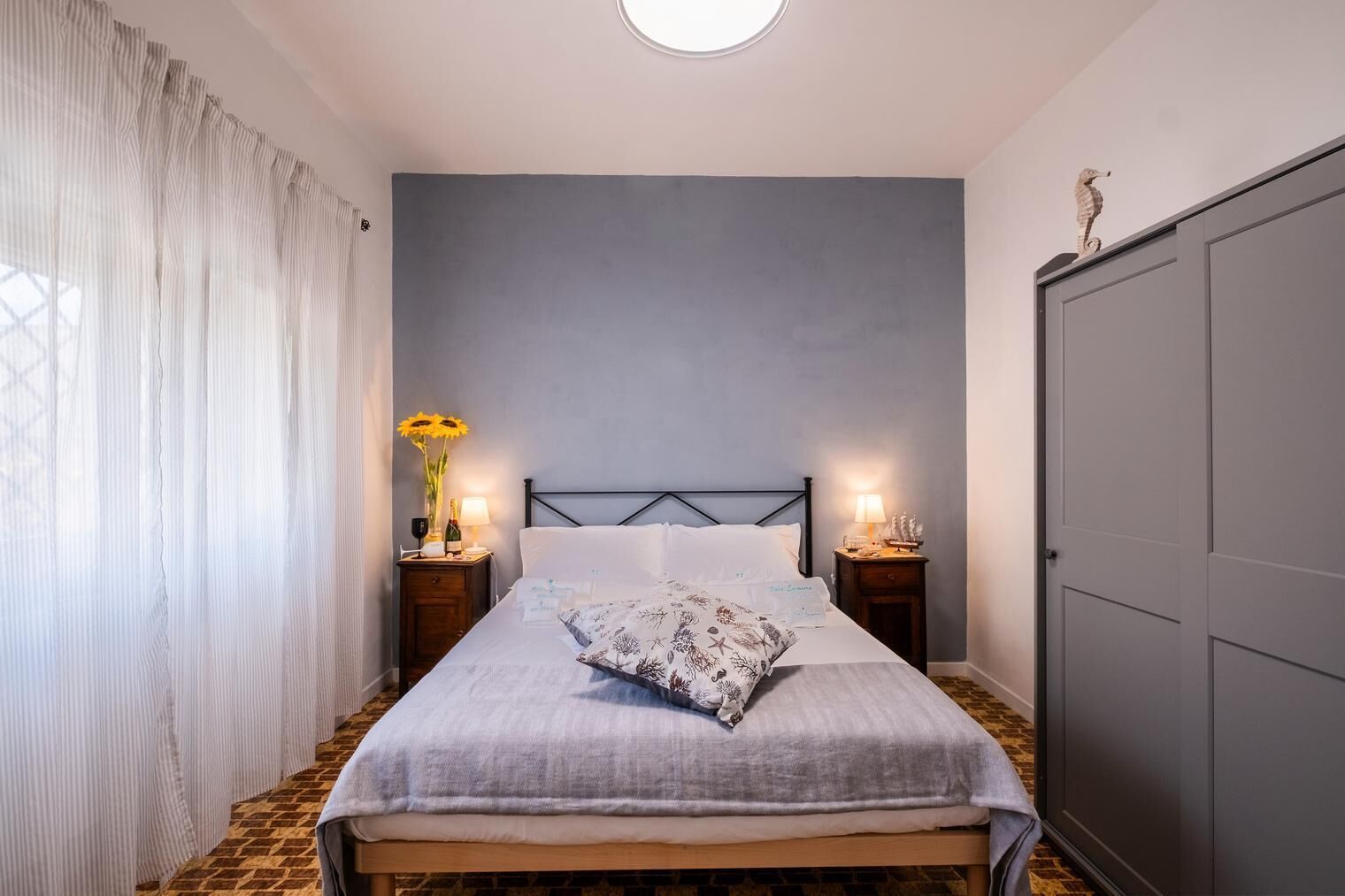 Un dormitorio ordenado con cama, dos mesitas de noche, un armario y una ventana con cortinas.