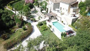 Vista aèria d'una propietat amb piscina, edifici de pedra i jardí amb diverses plantes i un camí.