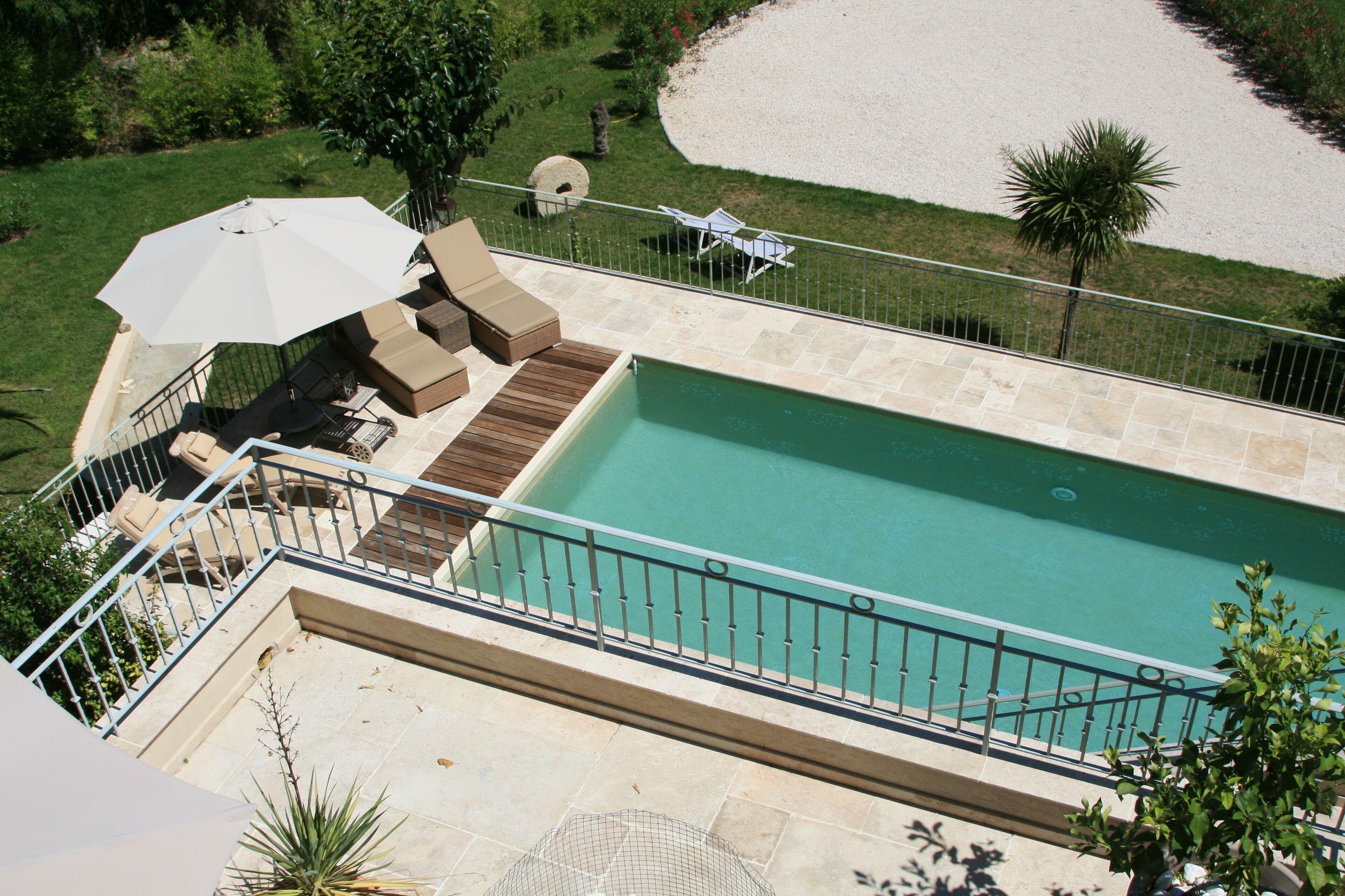 A rooftop pool area with a view of the surrounding landscape, including a lawn and a palm tree.