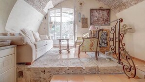 Un saló tranquil i acollidor amb un sostre alt i corbat, un sofà blanc, una taula petita i una escala amb barana de metall ornamentada.