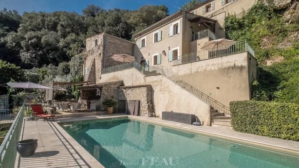 Zona de piscina amb un edifici de pedra, un pont de fusta i una escala que condueix a un segon pis.