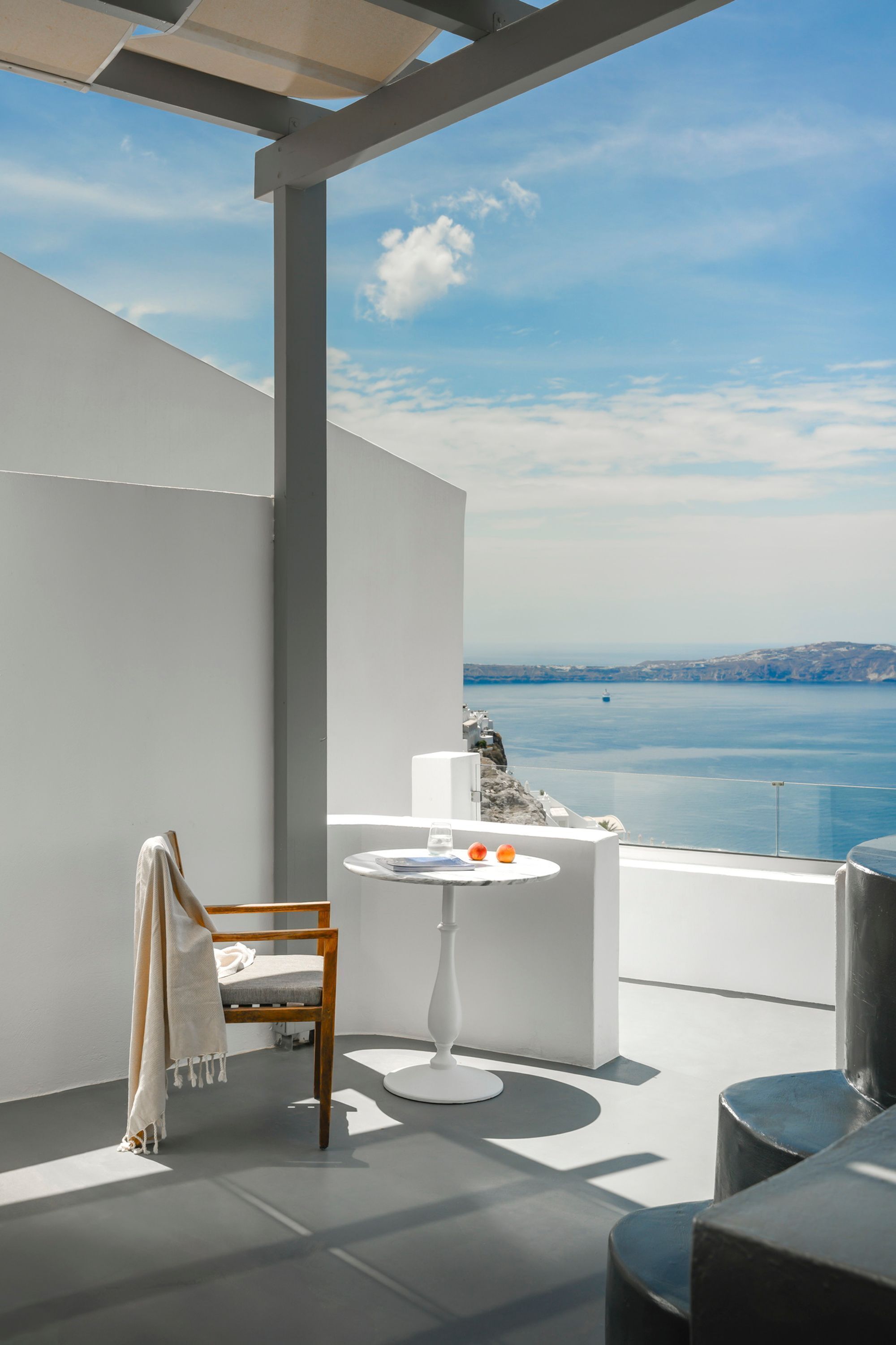 Un balcon moderne avec une chaise blanche, une petite table ronde et une vue sur la mer.