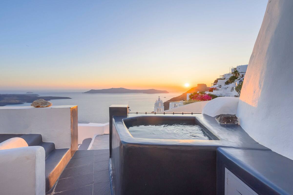 Una terraza con vistas al mar y al atardecer, que incluye una fuente de agua y arquitectura blanca.