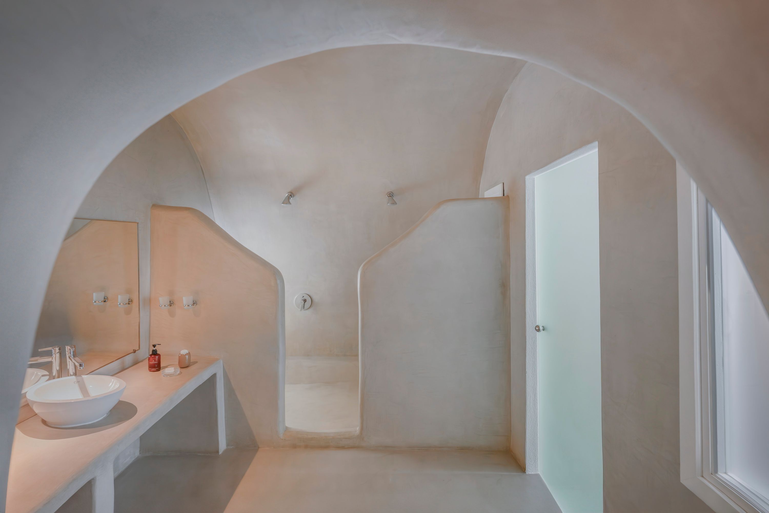 Un bagno moderno con un ampio soffitto ad arco, un lavandino bianco e uno spazio doccia in vetro.