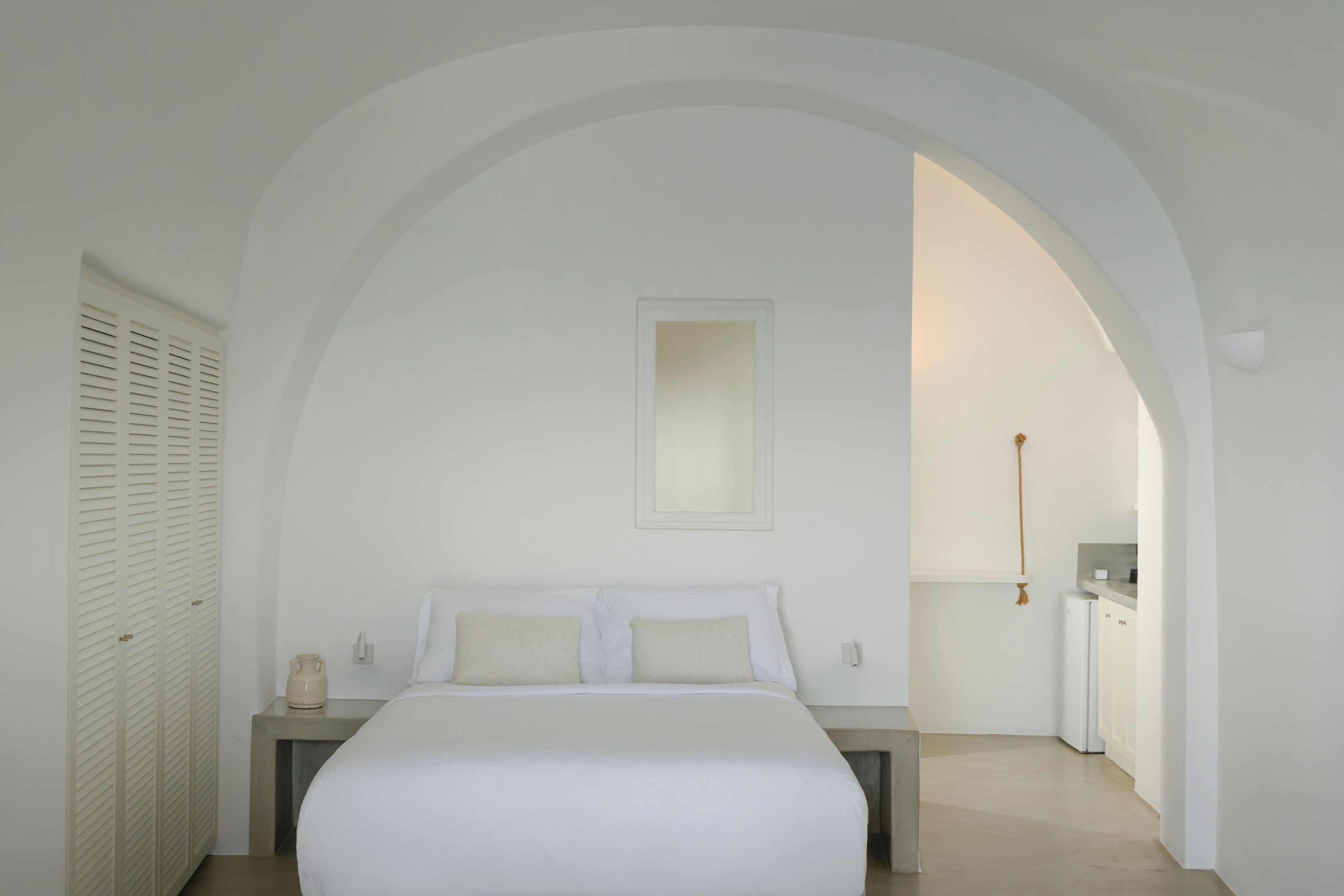Un dormitorio con cama, mesita de noche y un armario pequeño. Hay una puerta que da a un baño y una kitchenette.