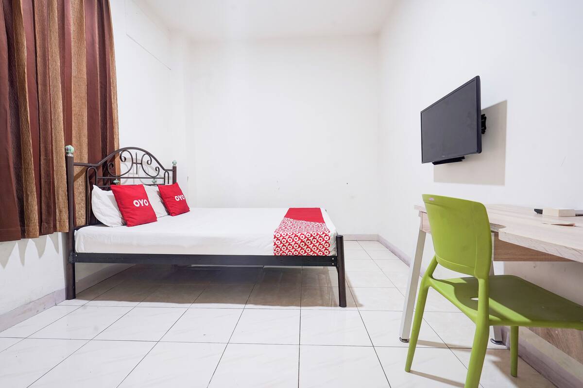 A small, neatly arranged room with a bed, a desk, and a chair.