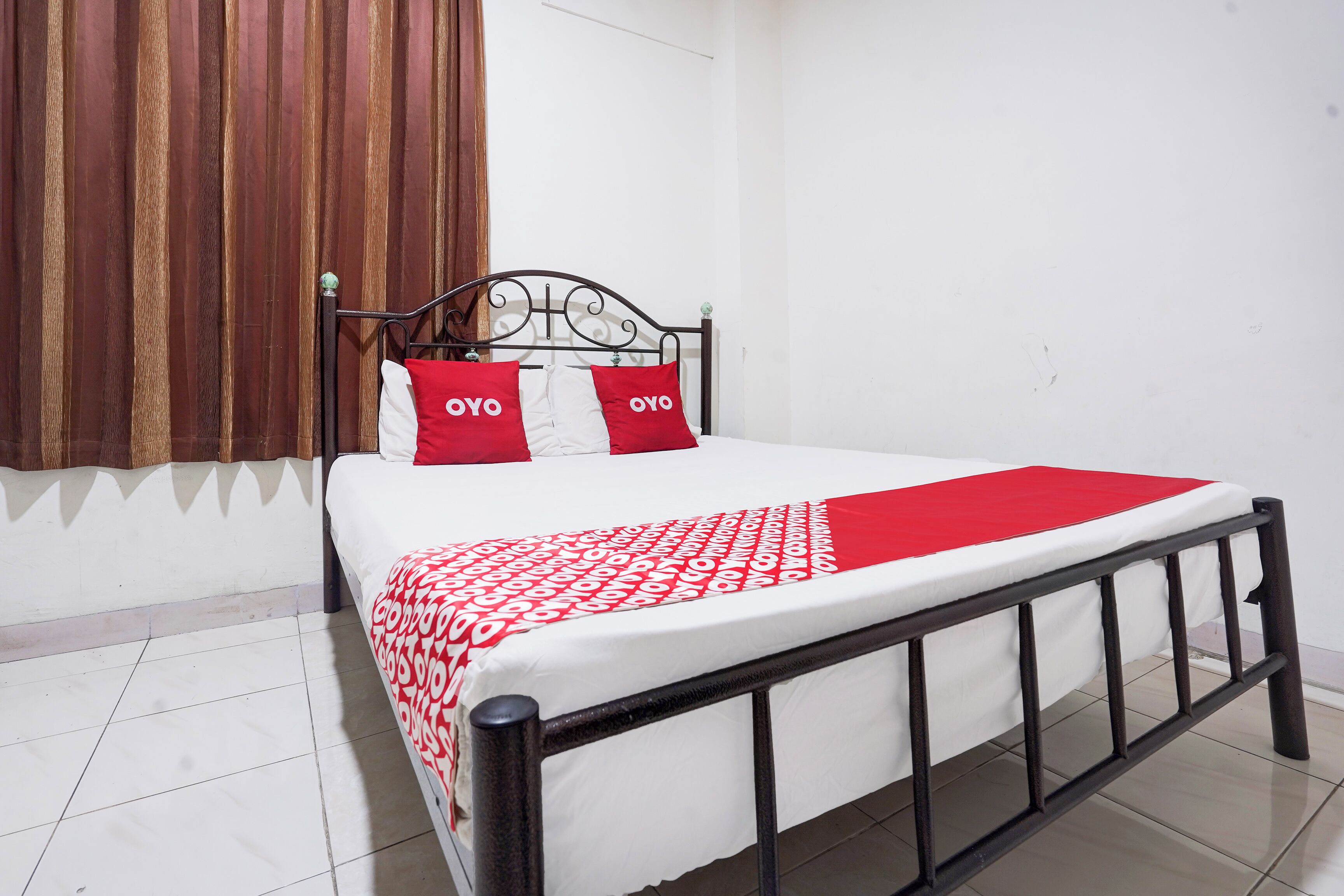 Un lit avec une couvre-lit à motifs rouges et blancs, deux oreillers rouges ornés de texte blanc et une tête de lit en métal noir.