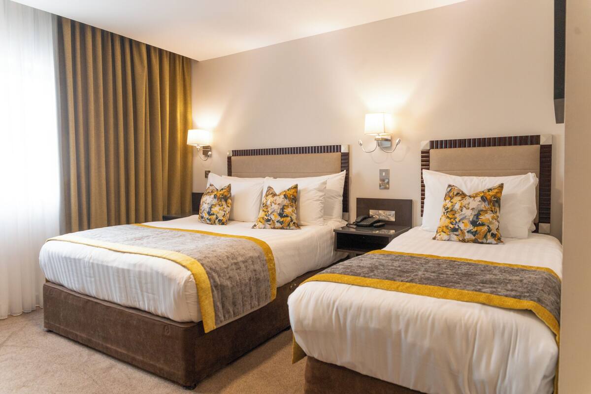 Una habitación de hotel con dos camas, cada una con cabecera, mesitas de noche, lámparas y almohadas decorativas.