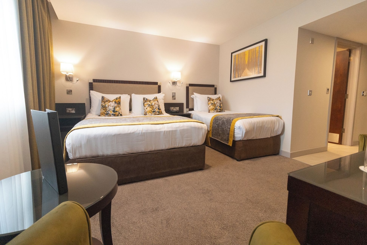 Quarto de hotel com duas camas, uma mesa e uma cadeira.