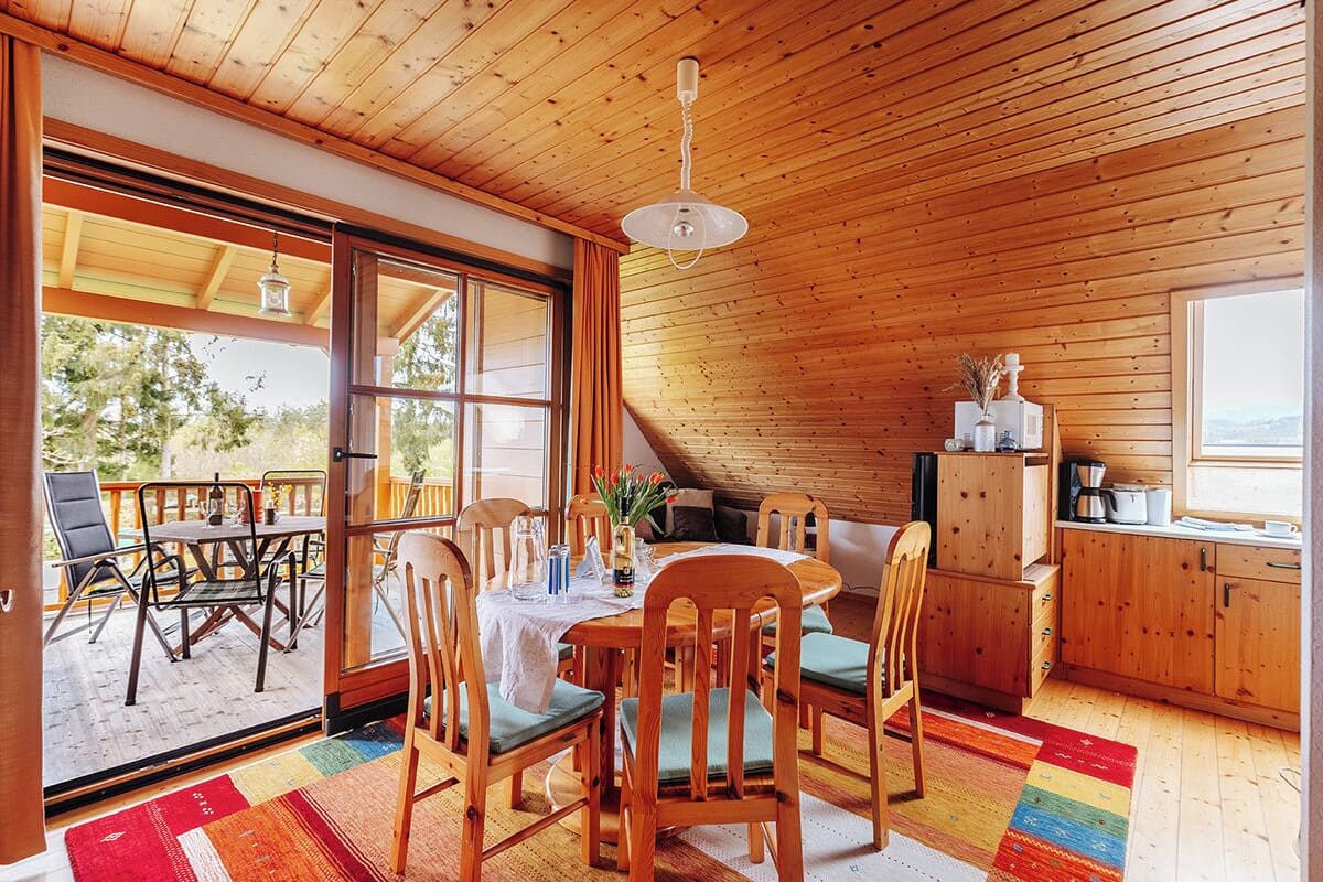 A cozy wooden interior with a dining area, kitchen, and large windows.