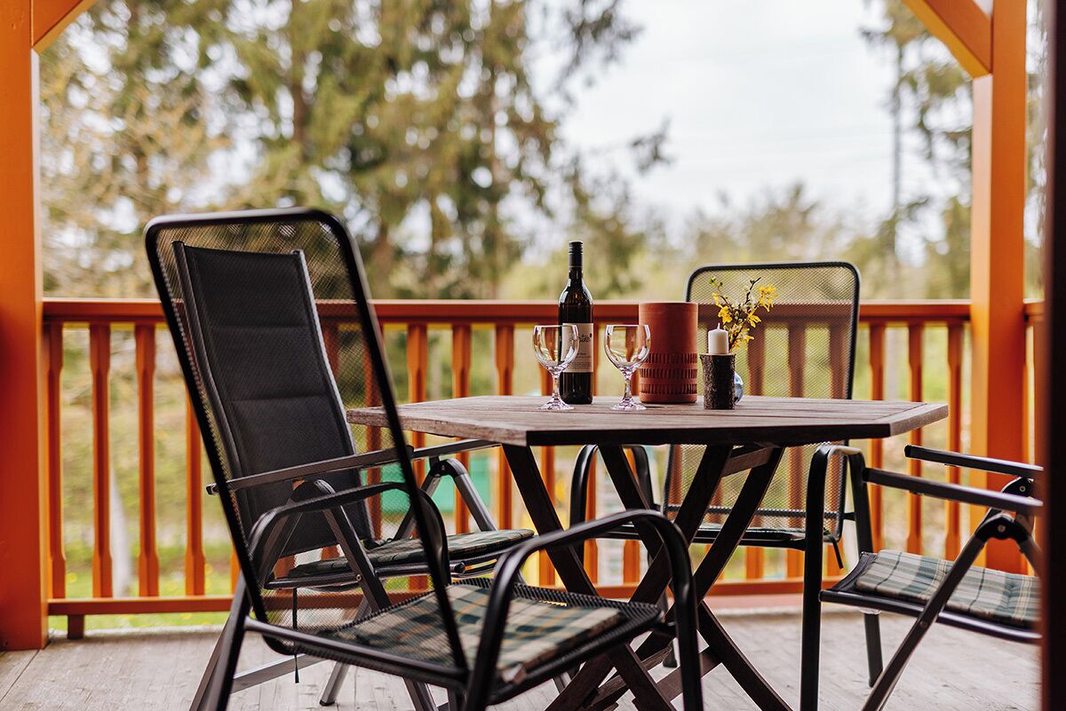 A wooden table with four chairs, a bottle of wine, and a vase with flowers on a balcony.