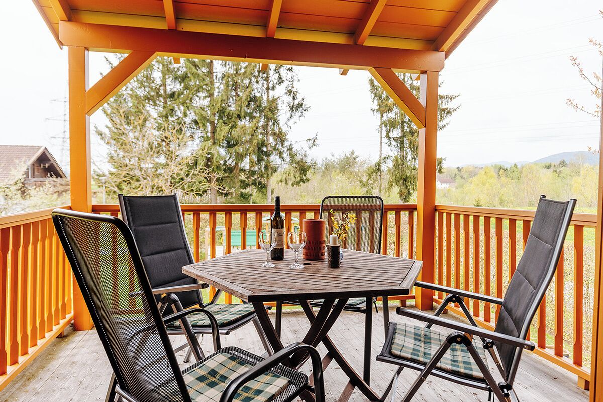 Eine Holzterrasse mit Tisch und vier Stühlen, einer Weinflasche und einer Kerze auf dem Tisch.