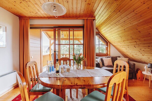 A cozy room with a wooden ceiling, a dining table with chairs, a sofa, and a window with curtains. - Ferienhaus Nora (Sankt Kanzian am Klopeiner See)