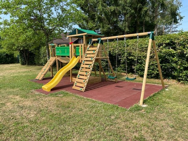 A wooden playground with a slide, climbing ladder, and swings.