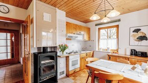 A modern kitchen with wooden cabinets, a built-in oven, a dining table with chairs, and a large window providing natural light. - Ferienhaus Nora (Sankt Kanzian am Klopeiner See)