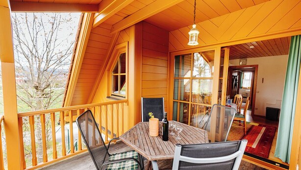 A wooden deck with a table and chairs, a hanging light fixture, and a view of the outdoors. - Ferienhaus Nora (Sankt Kanzian am Klopeiner See)