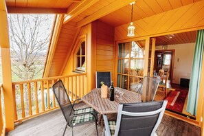 A wooden deck with a table and chairs, a hanging light fixture, and a view of the outdoors. - Ferienhaus Nora (Sankt Kanzian am Klopeiner See)