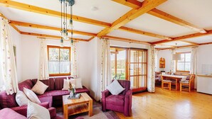 A spacious living room with a wooden floor, a sofa set, a dining table with chairs, and large windows allowing natural light. - Ferienhaus Nora (Sankt Kanzian am Klopeiner See)