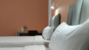 Ein Hotelzimmer mit zwei Betten, weißen Laken, einem Nachttisch mit Lampe sowie einem Tisch mit Wasserflaschen.