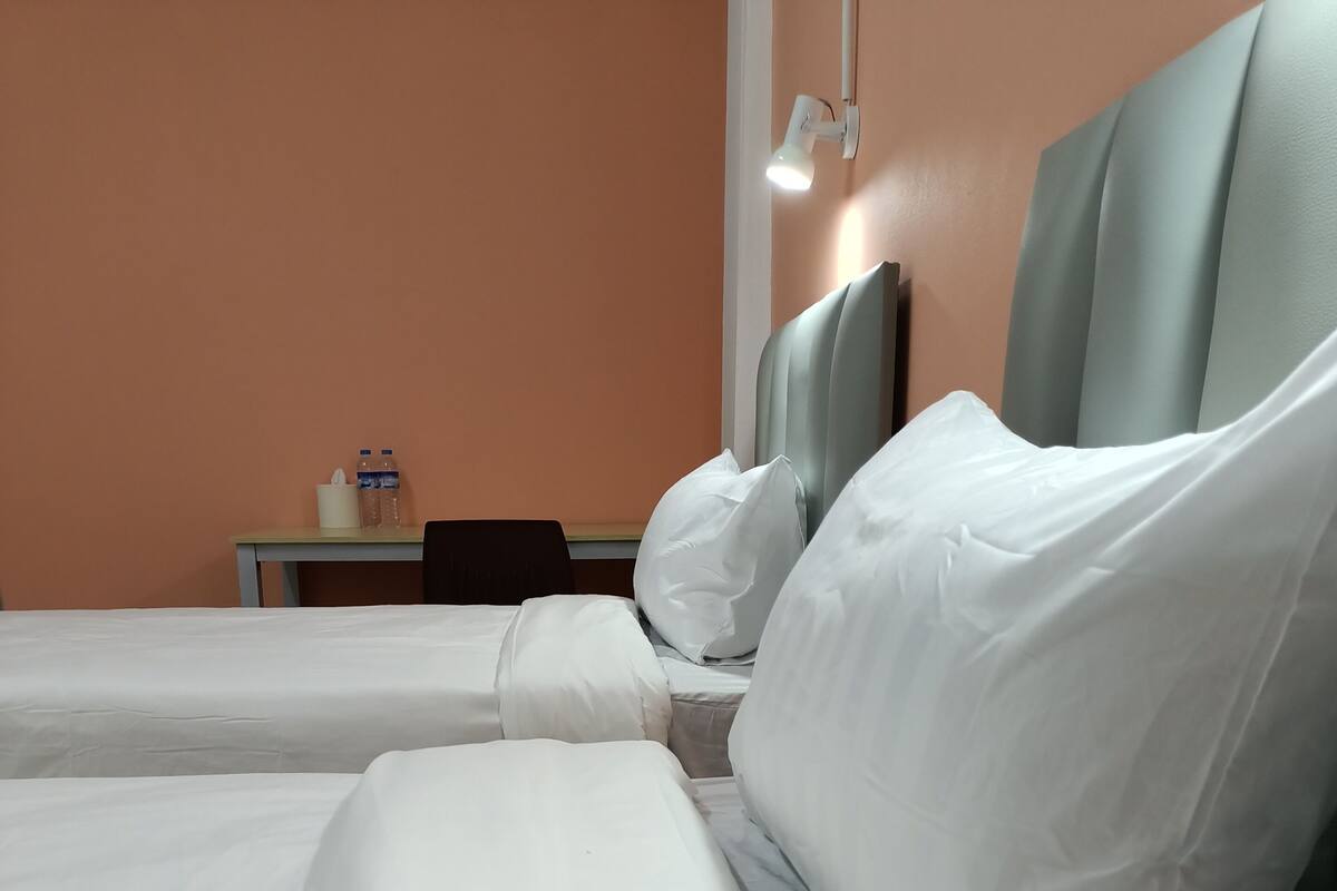 A hotel room with two beds, white linens, a nightstand with a lamp, and a table with water bottles.